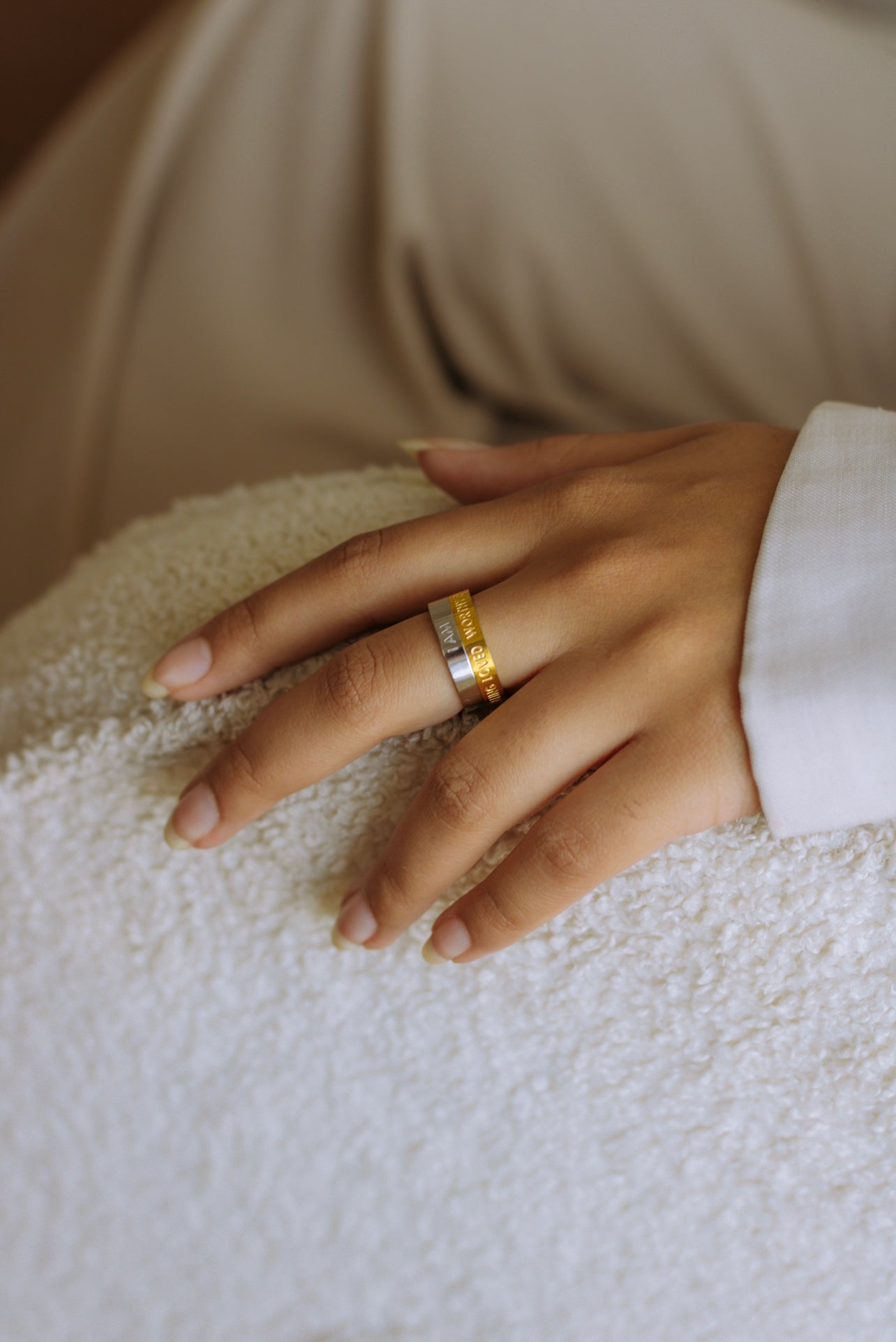 A person's hand wearing a two toned rotating affirmation ring set against a neutral background.
